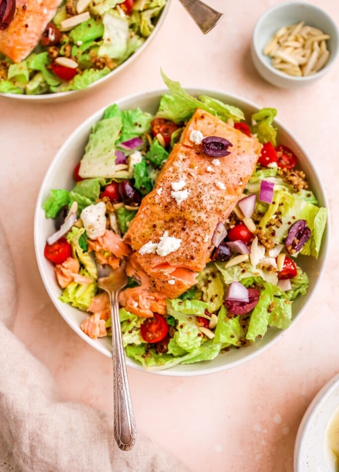 A bowl with mediterranean salad topped with a filet of salmon.