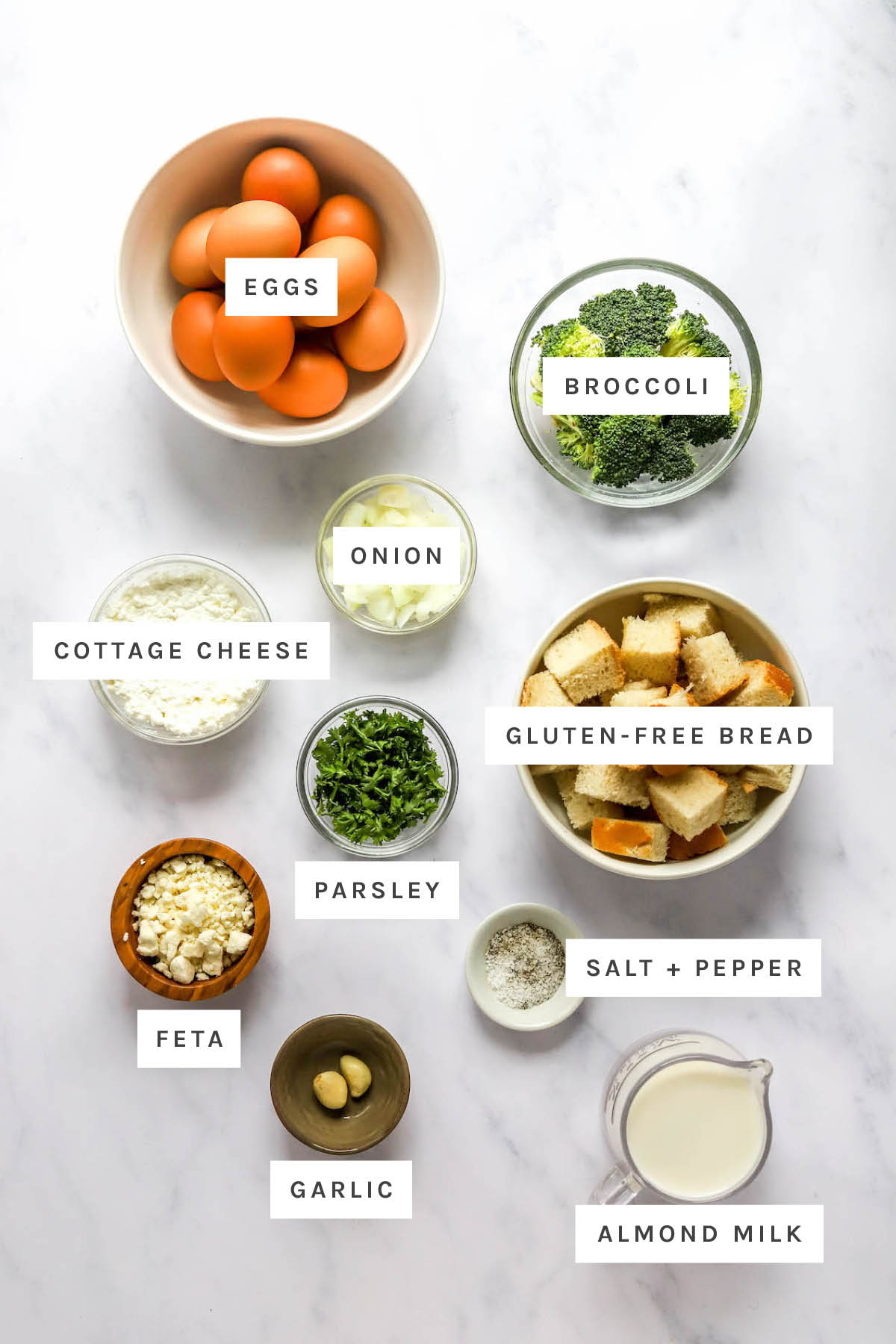 Save this healthy breakfast casserole! Ingredients measured out to make a healthy breakfast casserole: eggs, broccoli, onion, cottage cheese, gluten-free bread, parsley, feta, garlic, almond milk, salt and pepper.