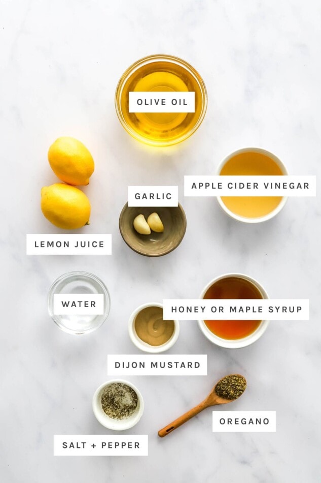 Ingredients measured out to make lemon dressing: olive oil, lemon juice, vinegar, garlic, water, honey or maple syrup, dijon mustard, oregano, salt and pepper.