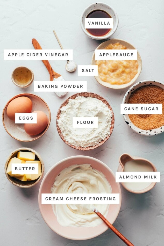 Ingredients measured out to make vanilla cupcakes: vanilla, applesauce, salt, vinegar, baking powder, cane sugar, flour, eggs, butter, almond milk and cream cheese frosting.