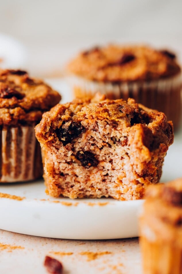 Carrot Raisin Muffins with Coconut Butter Drizzle A carrot raisin muffin on a plate. A bite has been taken from the muffin.