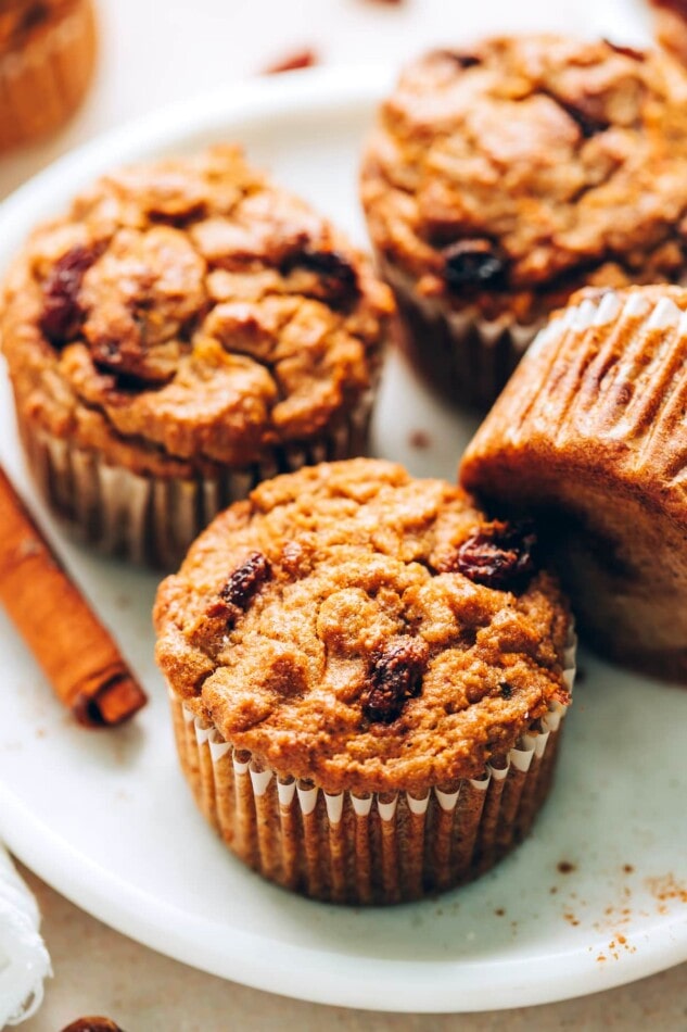 Grain-free carrot raisin muffins made with almond and coconut flour. Loaded with cinnamon flavor and studded with raisins, these moist muffins are sweet without being too sweet and lovely topped with a little coconut butter. An angled photo of 4 carrot raisin muffins on a plate. One of the muffins is resting on it's side.