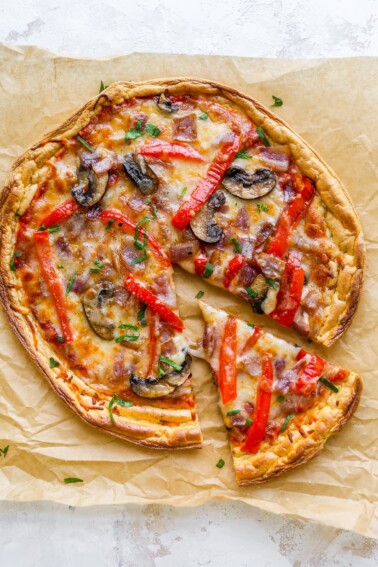 An overhead view of cloud bread pizza on a sheet of brown parchment paper. A slice has been cut and slightly removed from the pizza.