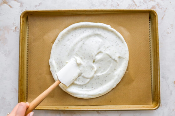 Spreading egg white mixture onto a baking sheet covered with a sheet of brown parchment paper.