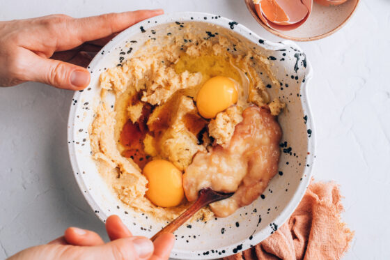 Eggs, applesauce and vanilla extract added to the sugar and butter mixture in a bowl.