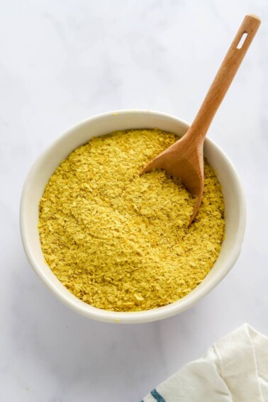 A small bowl with nutritional yeast and a small wooden serving spoon.
