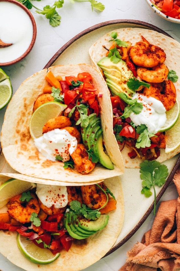These sheet pan shrimp fajitas make for an easy weeknight meal with Mexican flavor. Simply bake your shrimp, peppers and onions together on one sheet, load up your tortillas and enjoy! Three fajitas on a serving platter.