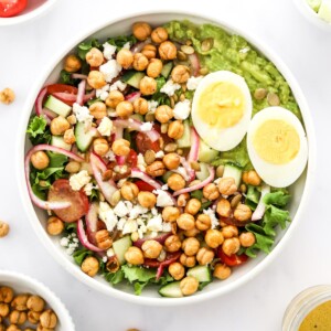 A large bowl of cooked chickpeas, hard boiled egg, lettuce, red onion, feta cheese, cherry tomatoes, and avocado.