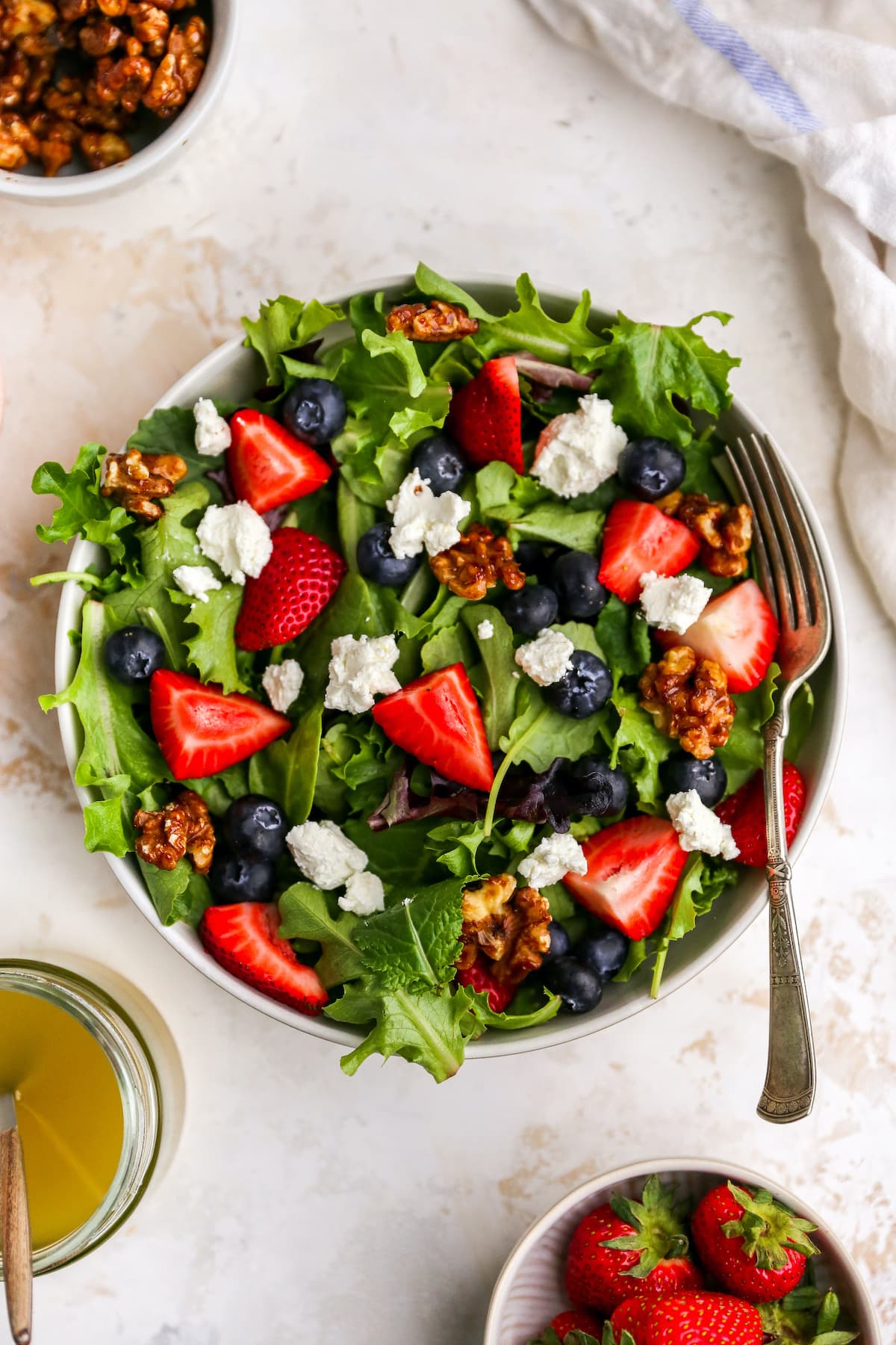Patriotic berry salad loaded with fresh berries, crunchy maple walnuts and blue cheese. The red white and blue theme makes it perfect for the 4th of July. A bowl with summer berry salad. A fork rests on bowl.