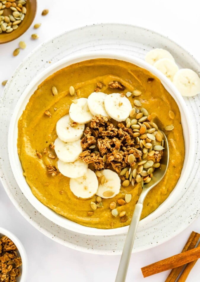 Fall Inspired Pumpkin Pitaya Bowl with pumpkin, pomegranate and granola. A pumpkin smoothie bowl topped with pumpkin seeds, granola and banana slices.
