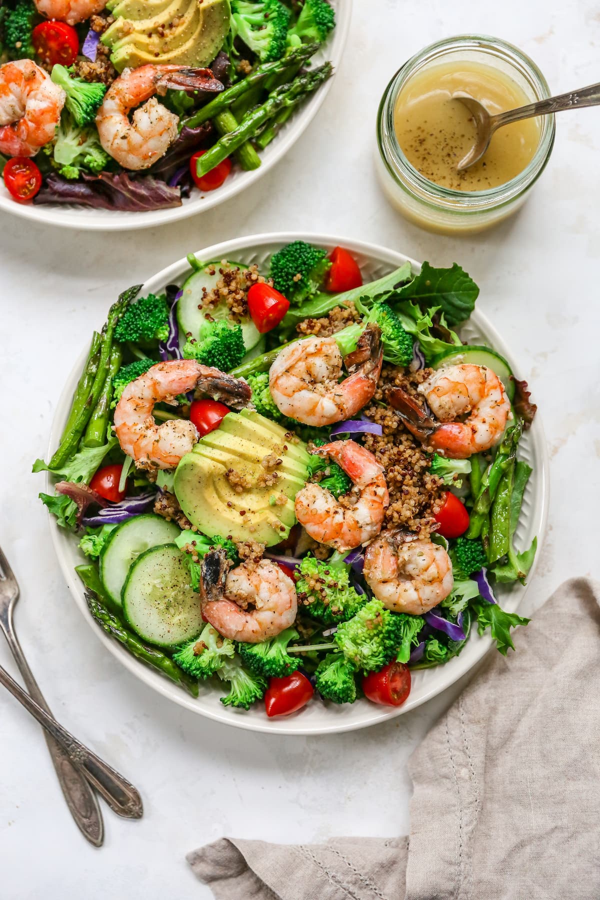 A clean eating shrimp salad with cooked shrimp, quinoa, blanched broccoli and roasted asparagus! Prepare everything ahead of time and throw it into a bowl for a quick and easy lunch or dinner. Overhead photo of a bowl of grilled shrimp salad.