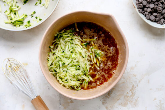 Eggs, maple syrup and vanilla extract in a bowl with shredded zucchini added to it.