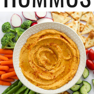 Sweet potato hummus in a serving bowl surrounded by veggies and pita for dipping.