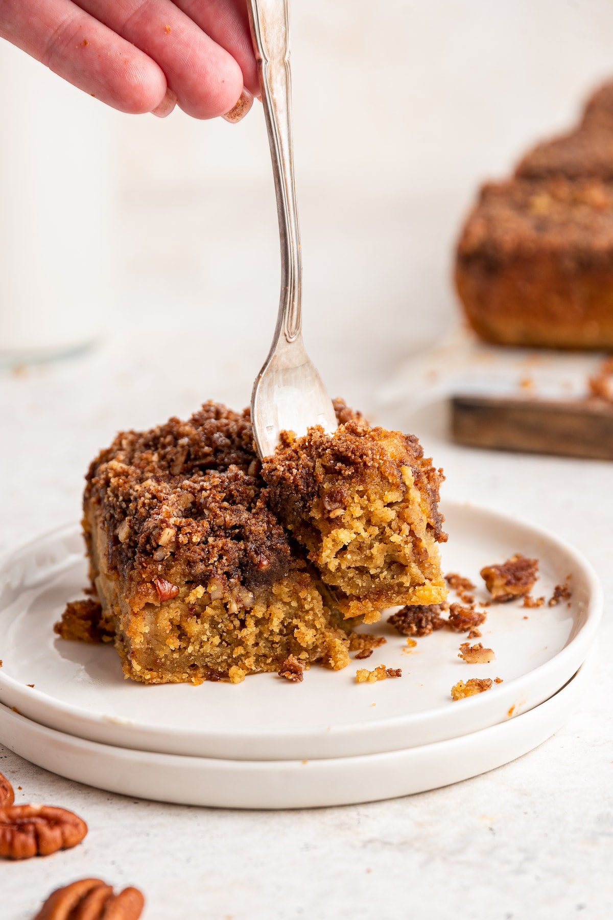 Forking removing a bite from a slice of apple cake on a plate.