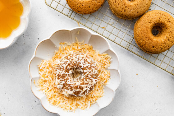 A donut, after being dipped into honey, now dipped in toasted coconut flakes.