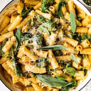 Creamy pumpkin pasta in a pot topped with fresh sage, pepitas and cheese.