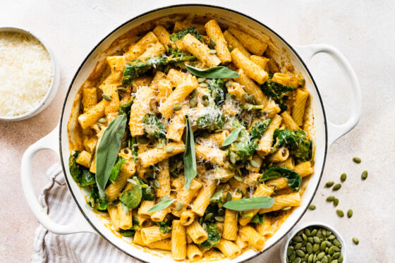 Pumpkin pasta in a pot topped with fresh sage, cheese and pepitas.
