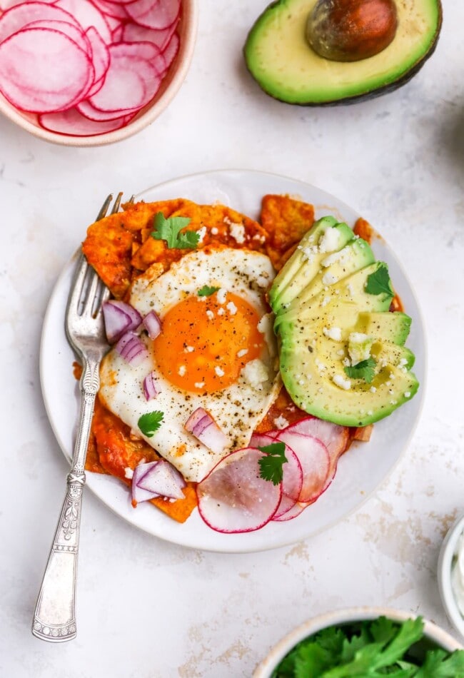 Chilaquiles with an egg and avocado on a plate with a fork.
