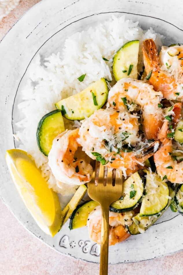 Overhead view of a plate with rice and a serving of shrimp scampi. A fork is spearing a shrimp.