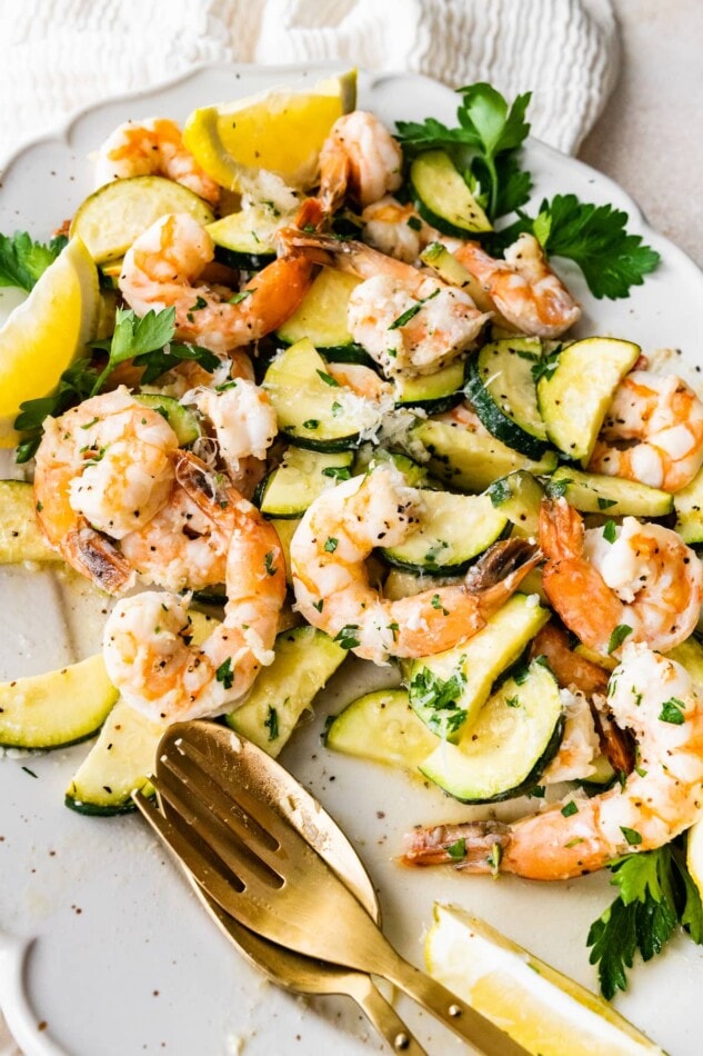 Shrimp scampi on a serving platter with a gold fork and spoon.