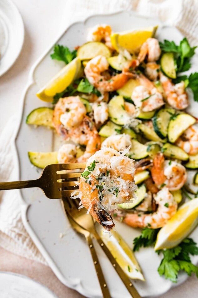 A fork holding up a shrimp over a platter of shrimp scampi.