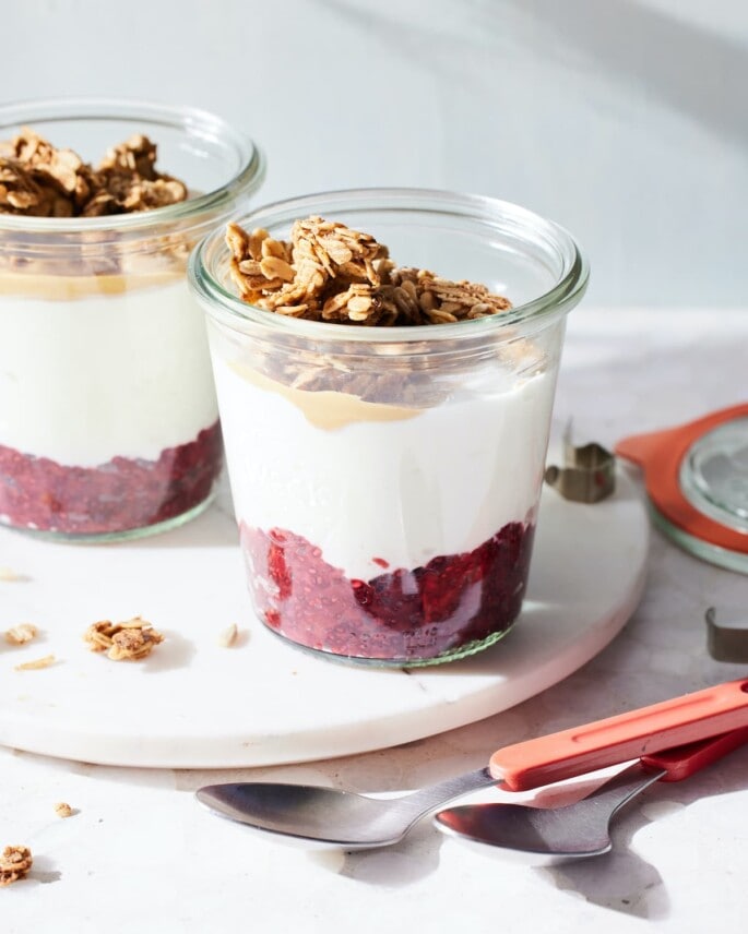 Two glass cups with a jelly, yogurt, peanut butter, and granola layering.