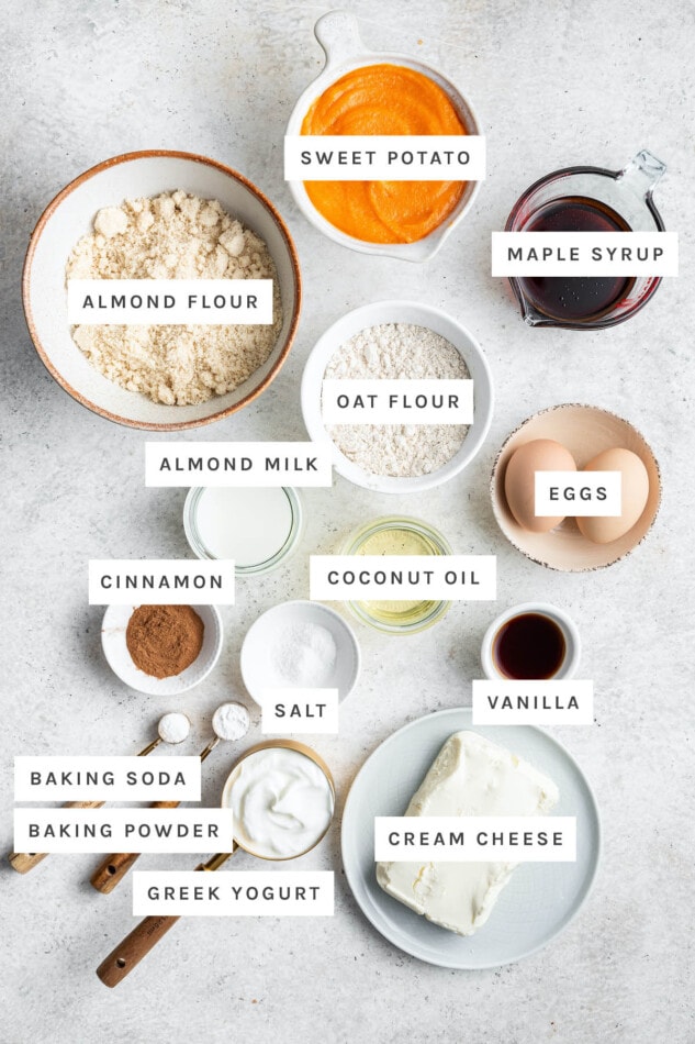 Ingredients measured out to make sweet potato muffins: sweet potato, maple syrup, almond flour, oat flour, eggs, almond milk, coconut oil, cinnamon, salt, vanilla, baking soda, baking powder, Greek yogurt and cream cheese.