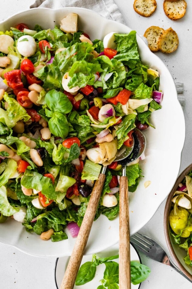 Vegetarian antipasto salad in a serving bowl with wooden serving utensils.