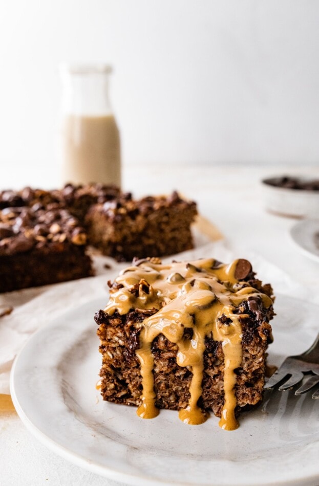 A serving of baked oatmeal on a plate with a peanut butter and maple syrup drizzle.