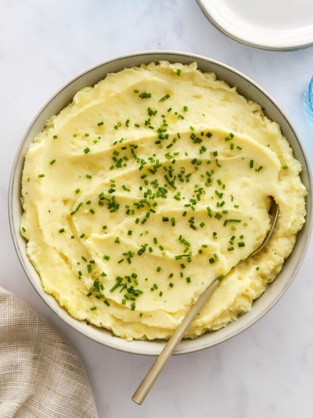 A large bowl of mashed potatoes, chives, and a metal spoon.