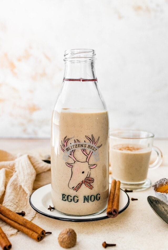 A simple recipe for dairy-free eggnog! Almond and coconut milk, egg whites and pure maple syrup come together for a flavor that rivals the original. A jug and a glass of dairy free eggnog.