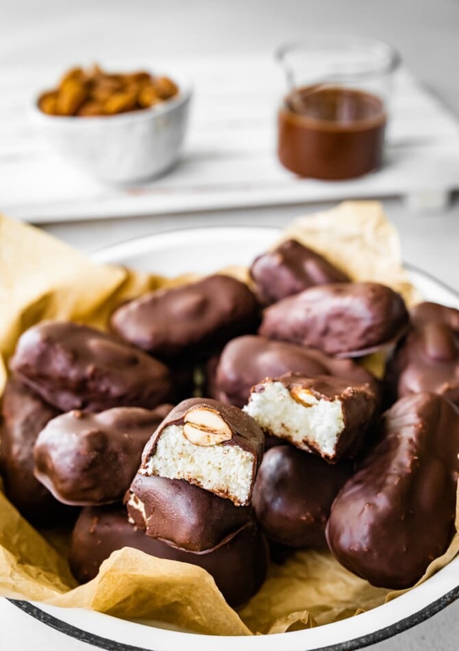 Homemade healthy almond joy bars in a bowl. One of the bars is sliced in half, exposing the coconut center.