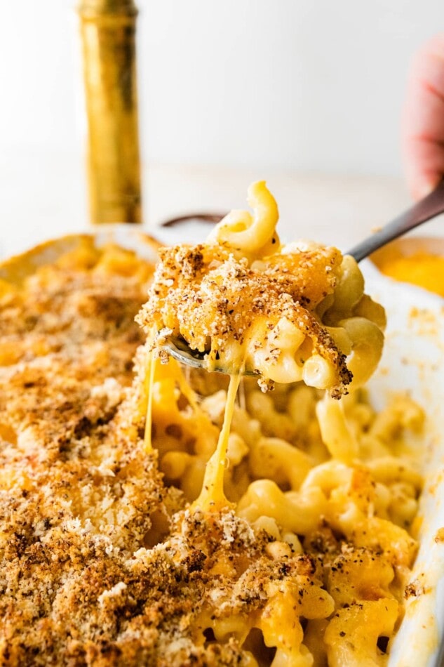 A spoonful of baked mac and cheese being removed from a larger baking dish.