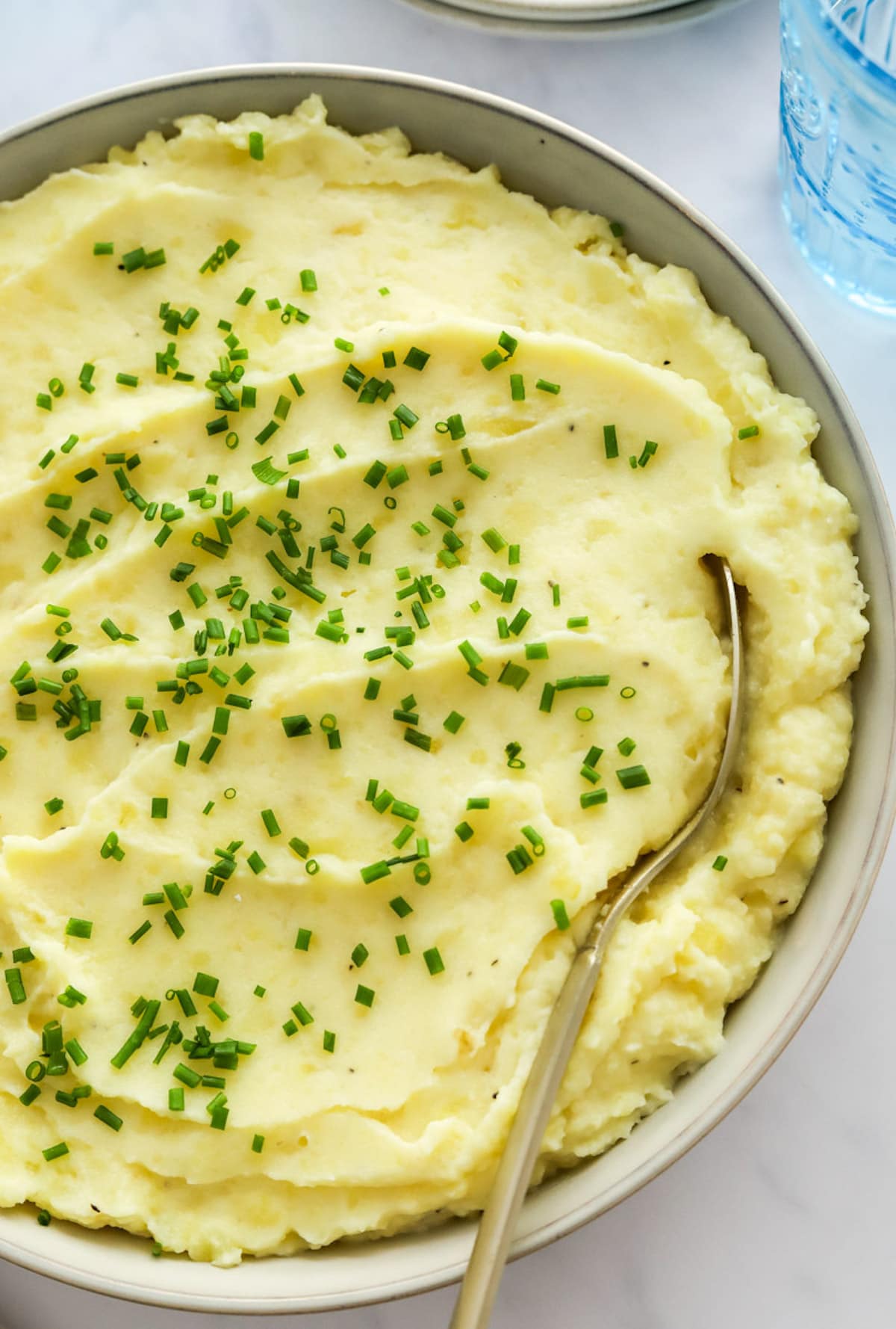 A large bowl of mashed potatoes topped with fresh chives and a metal spoon in the potatoes.