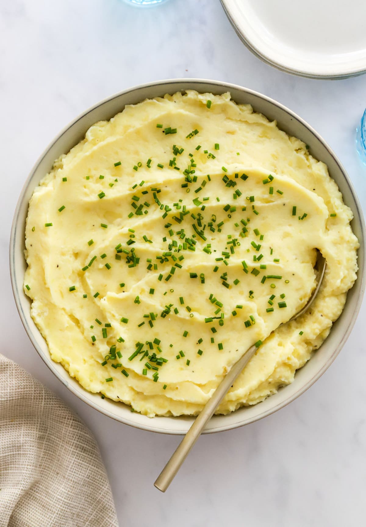 A large bowl of mashed potatoes garnished with fresh chives and a metal spoon in the mashed potatoes.