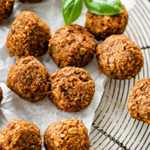 Vegan lentil meatballs with fresh basil on a cooling rack lined with parchment paper.