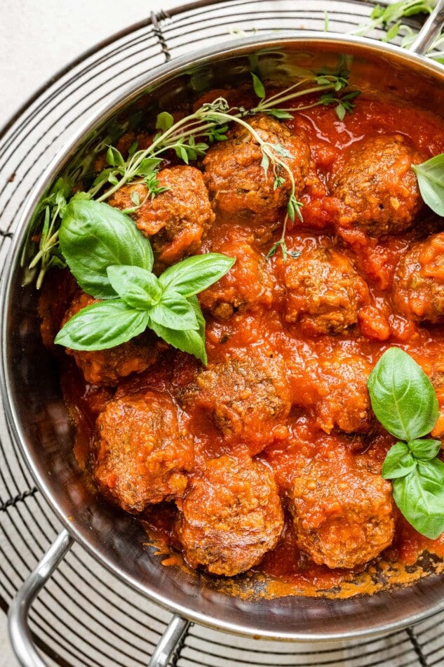 Vegan lentil meatballs, fresh basil and fresh time in a pot with sauce.