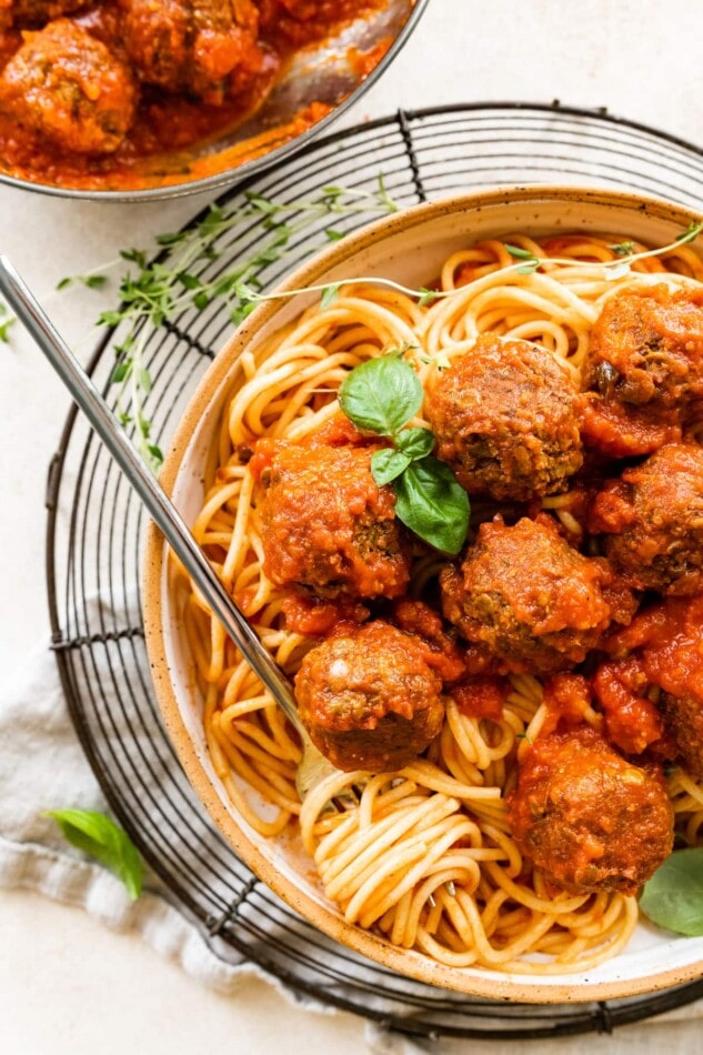 Lentil meatballs served over spaghetti noodles with fresh basil. Spaghetti noodles are twirled around a fork resting in the bowl.