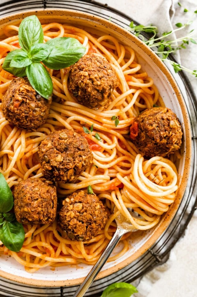 Lentil meatballs served over spaghetti noodles with fresh basil. Spaghetti noodles are twirled around a fork resting in the bowl.