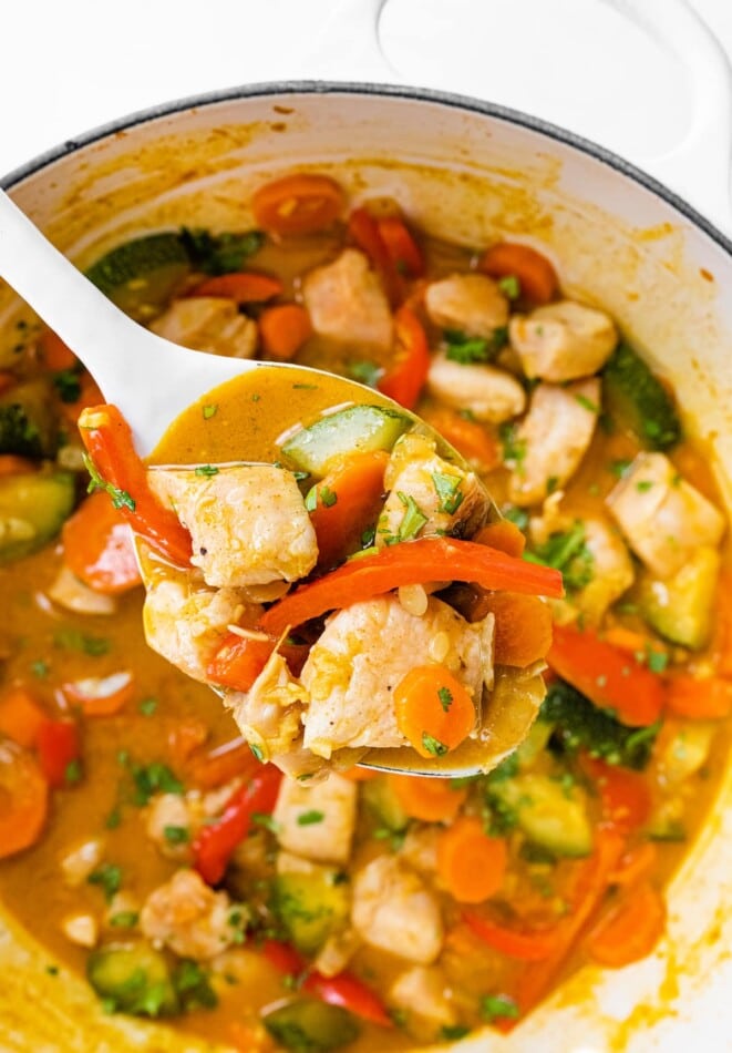 A serving spoonful of chicken curry with vegetables over a pot.