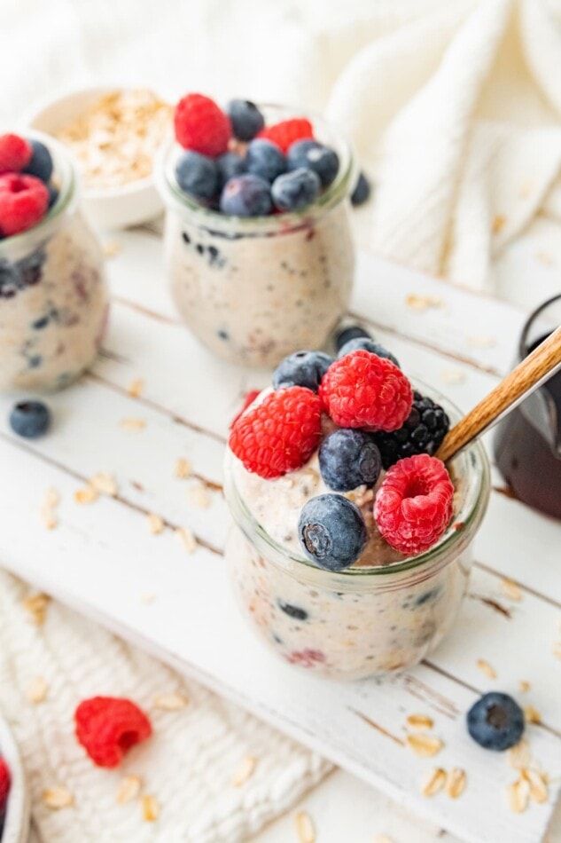 Three glass jars of overnight oats topped with fresh blueberries and raspberries.