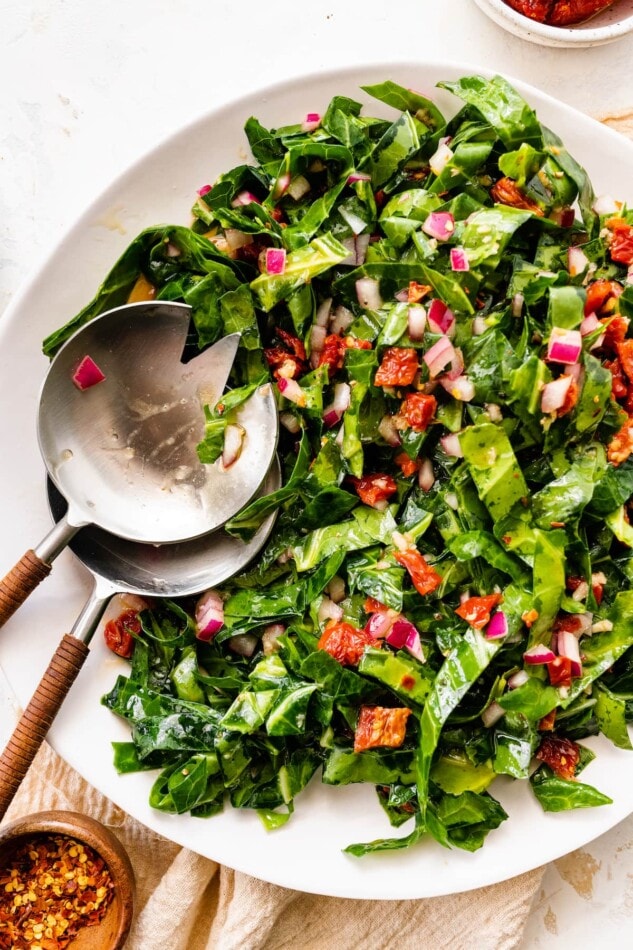Pin this image to save the recipe for this Raw Collard Greens Salad! A serving bowl containing raw collard greens salad with salad servers.