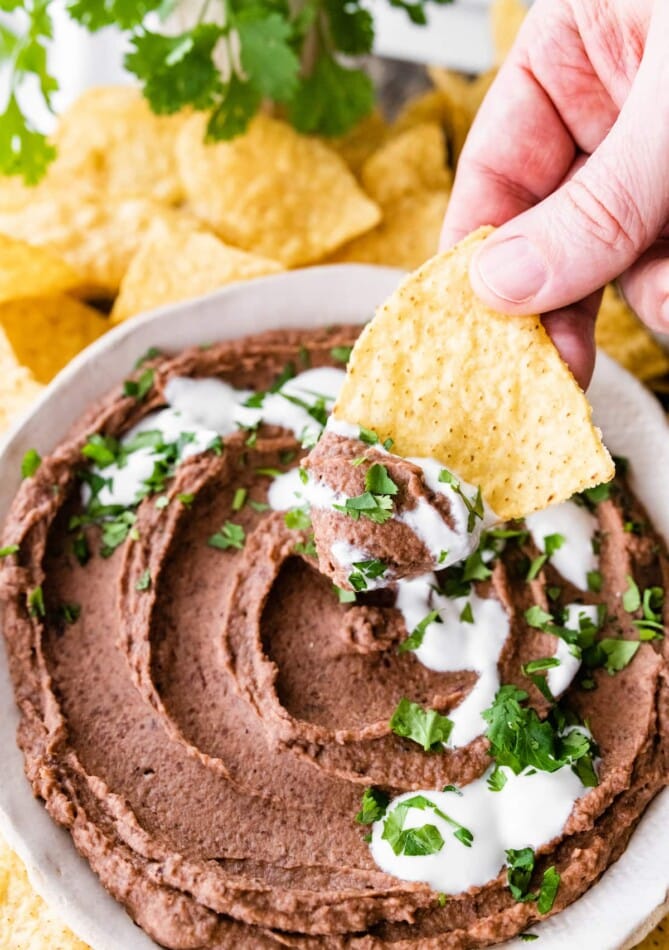 A hand scooping black bean dip onto a tortilla chip.