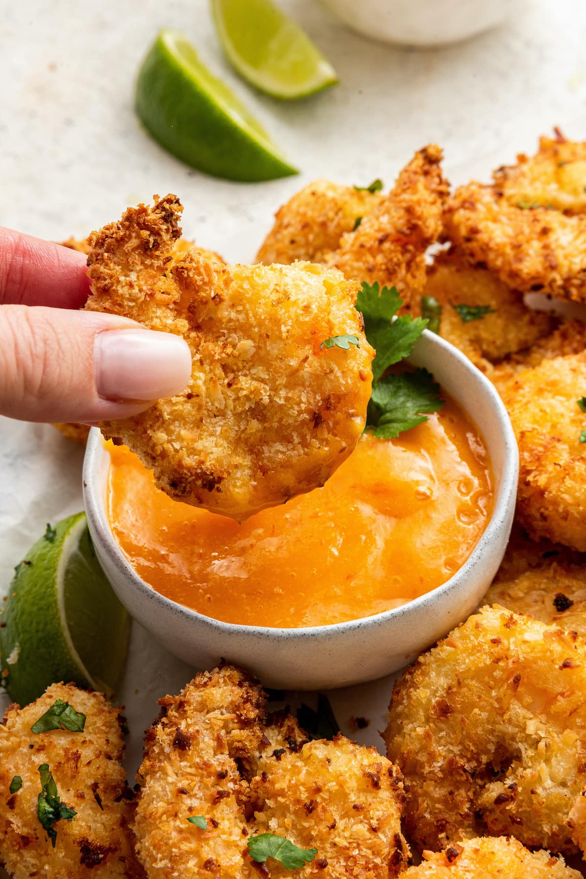 A hand dipping a coconut shrimp into sauce.