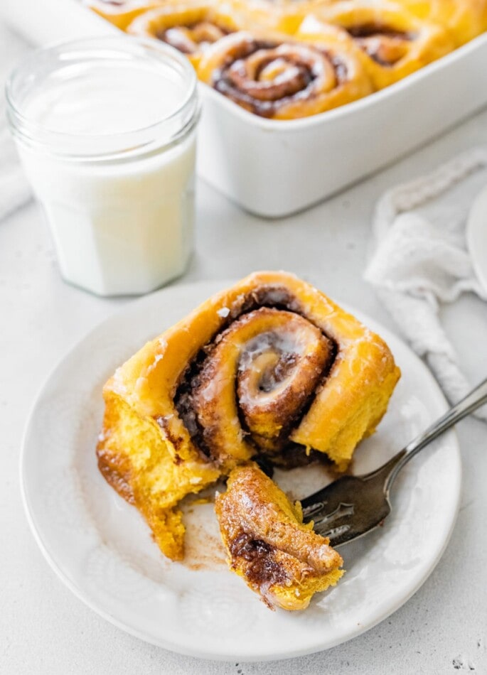 A pumpkin cinnamon roll on a plate with a fork.