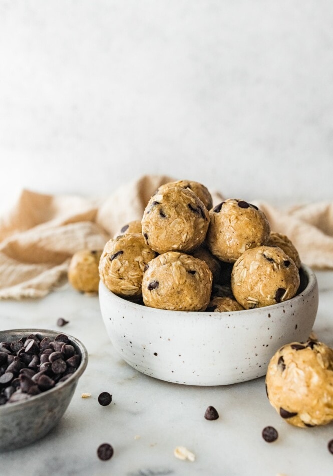A small bowl of tahini chocolate chip protein balls with other protein balls scattered around the counter top nearby.