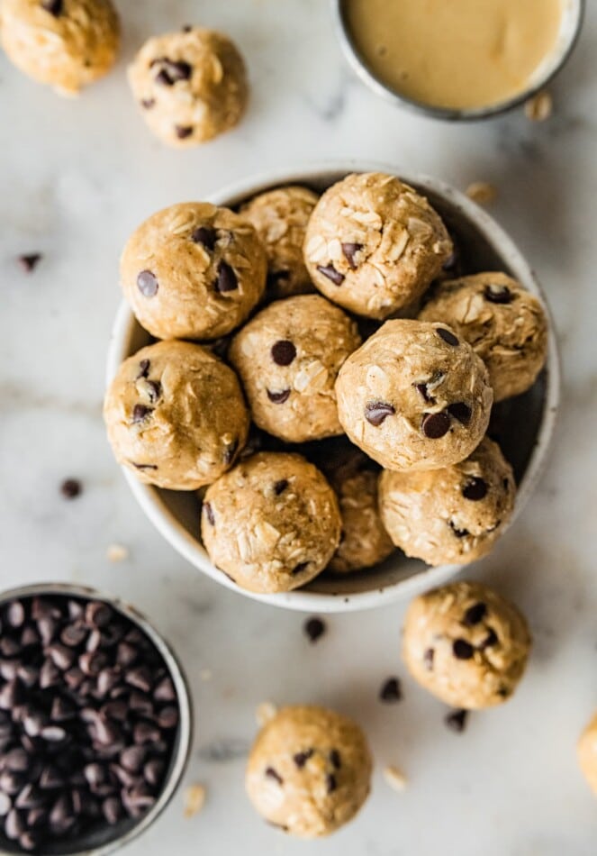 A bowl of tahini chocolate chip protein balls with another small bowl of chocolate chips nearby.