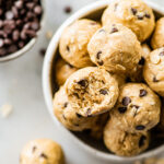 A bowl of tahini chocolate chip protein balls with one ball having a bite taken from it.