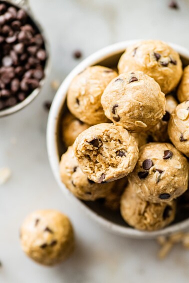A bowl of tahini chocolate chip protein balls with one ball having a bite taken from it.