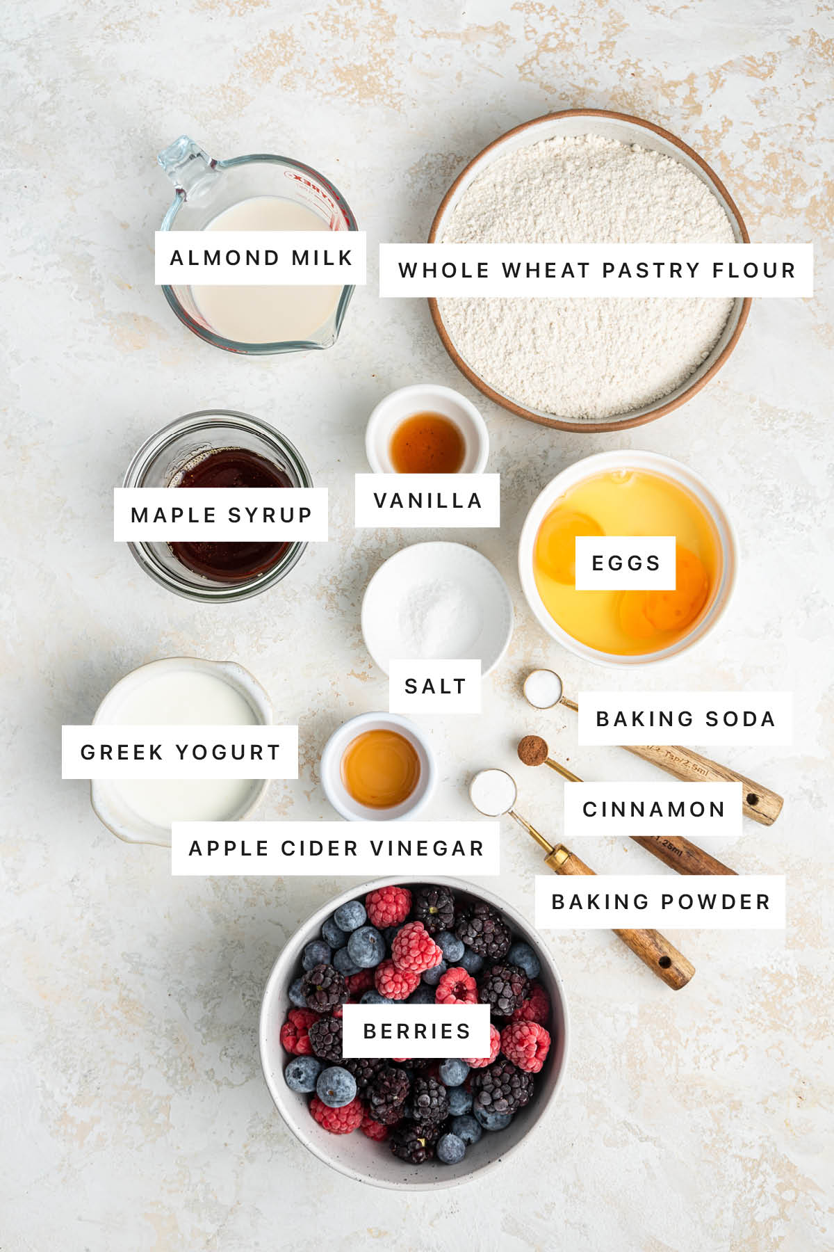 Ingredients used in an easy berry cake includes: eggs, whole wheat pastry flour, almond milk, vanilla, maple syrup, greek yogurt, salt, vinegar, cinnamon, baking soda, baking powder, and fresh berries.
